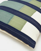 Close-up of a striped pillow with green, blue, and white colors on a light background