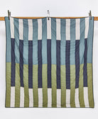 Striped quilt with blue, green, and white pattern on a wooden rack against a white background