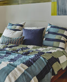 blue, green and white patchwork modern throw pillows on bed with matching quilt against a wall mural