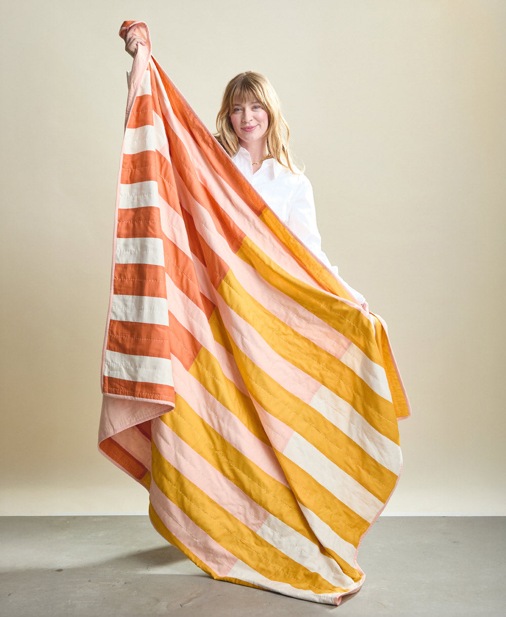 Woman holding a colorful striped blanket against a plain background