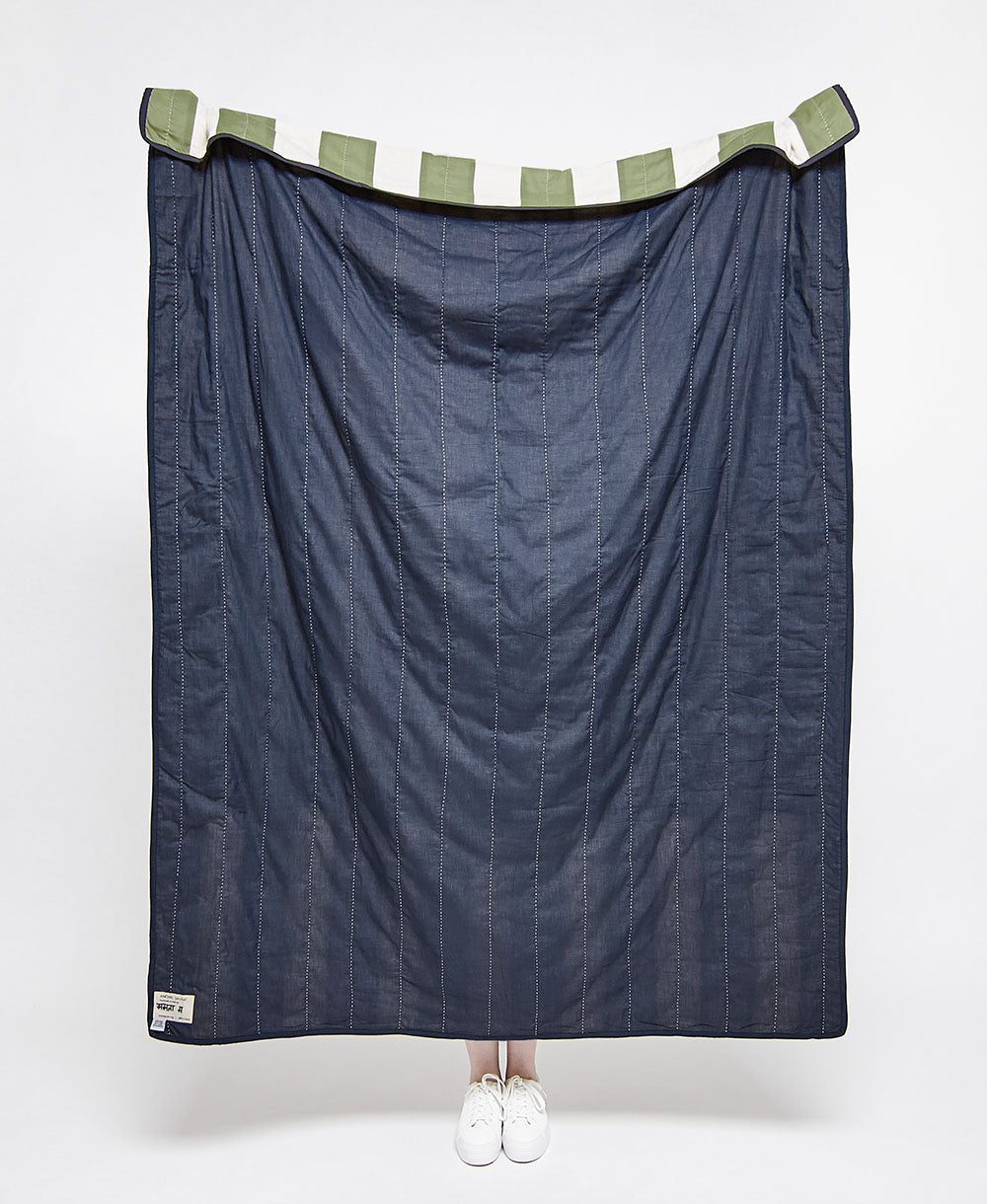 Blue striped quilt with green and white striped trim on a white background