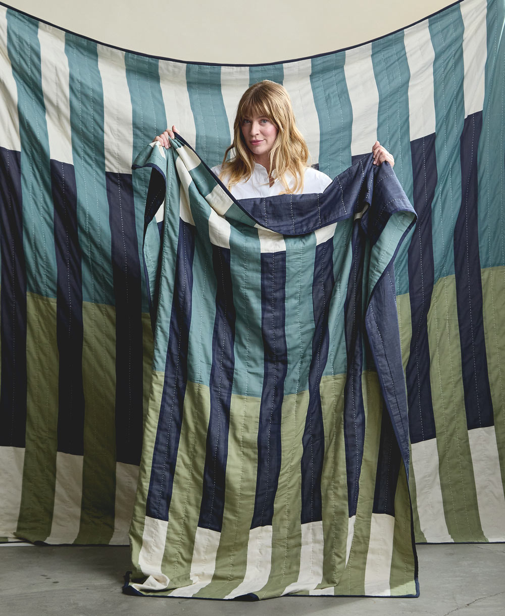 Woman holding a large striped quilt with green, blue, and white colors.