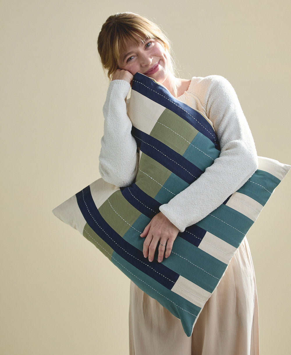 Woman holding a large bllue and green striped pillow against a plain background
