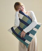 Woman holding a large bllue and green striped pillow against a plain background