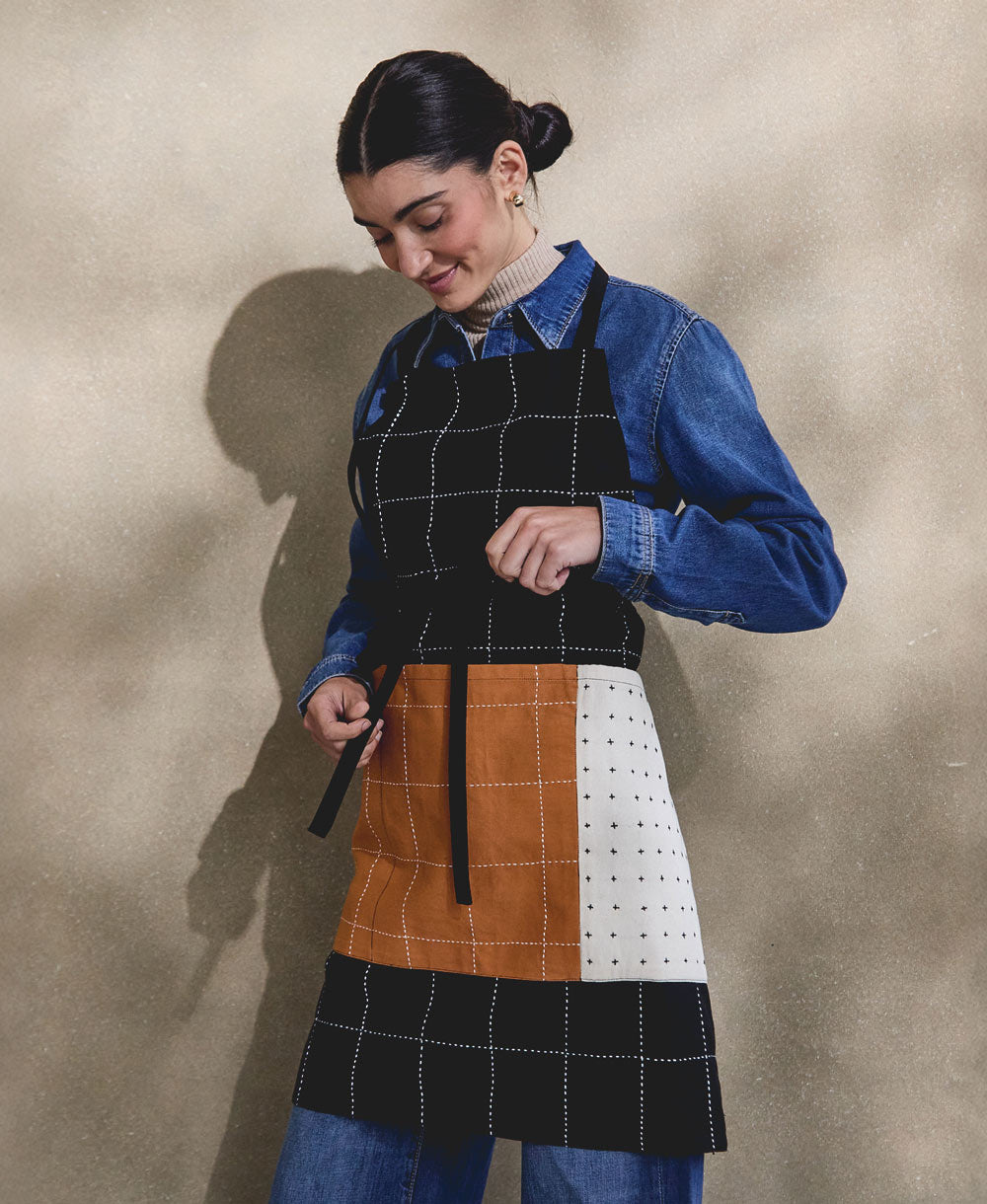 woman wearing a black, white and camel patchwork apron with a beige background