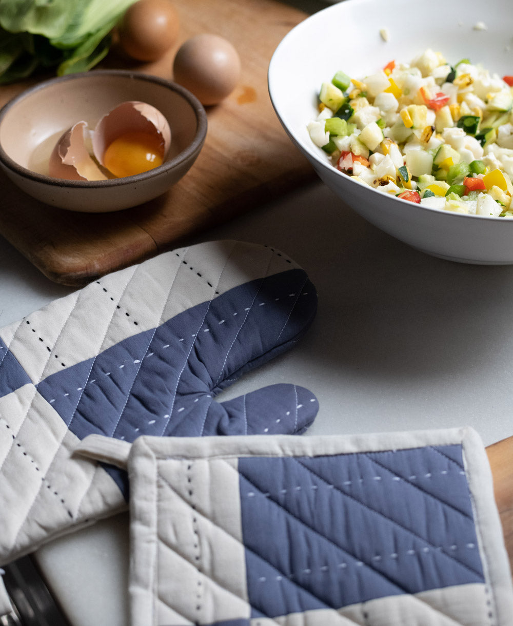 Cooking scene with a bowl of salad, eggs, and patchwork quilted oven mitts on a table