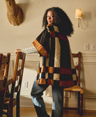 Woman wearing a patchwork quilted jacket in a room with wooden chairs and a lamp
