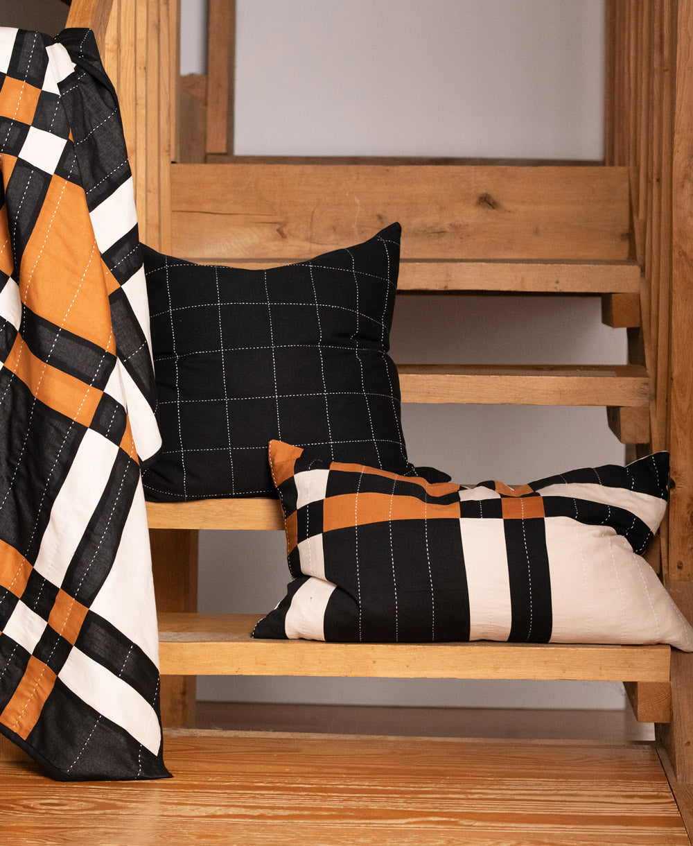 Black and white checkered pillow on a wooden stairwell with a plaid blanket