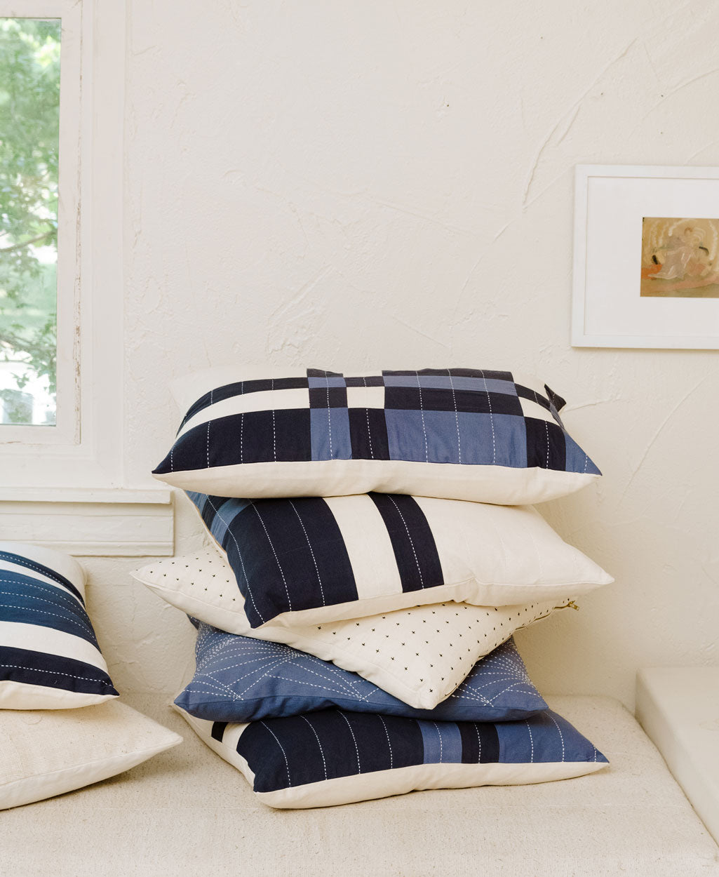 Stack of blue and white checkered pillows on a sofa near a window