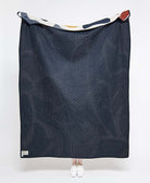 Dark blue quilt with geometric pattern draped over a person on a white background