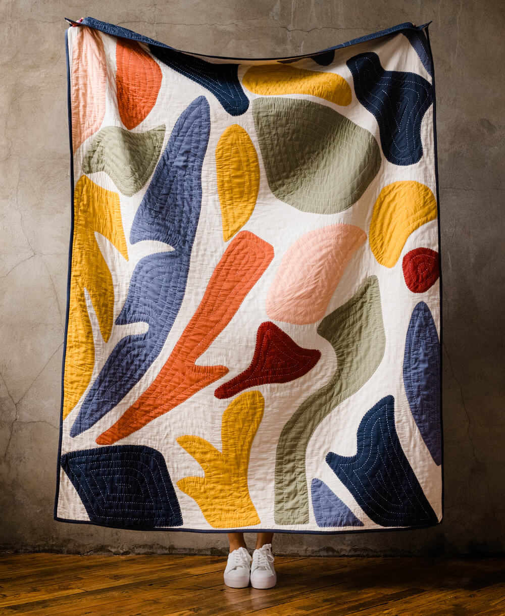 Colorful abstract-patterned quilt draped over a person against a neutral background