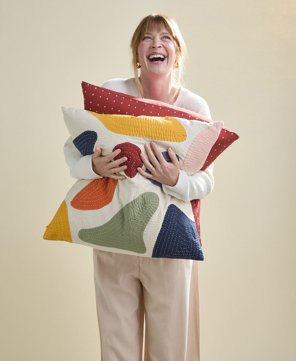 Woman holding a colorful geometric-patterned pillow against a plain background