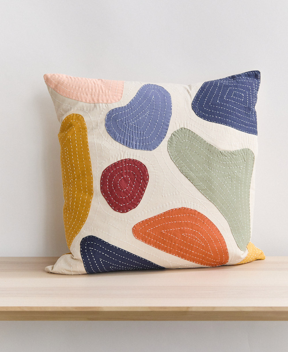 Colorful abstract-patterned pillow on a wooden surface with a light background