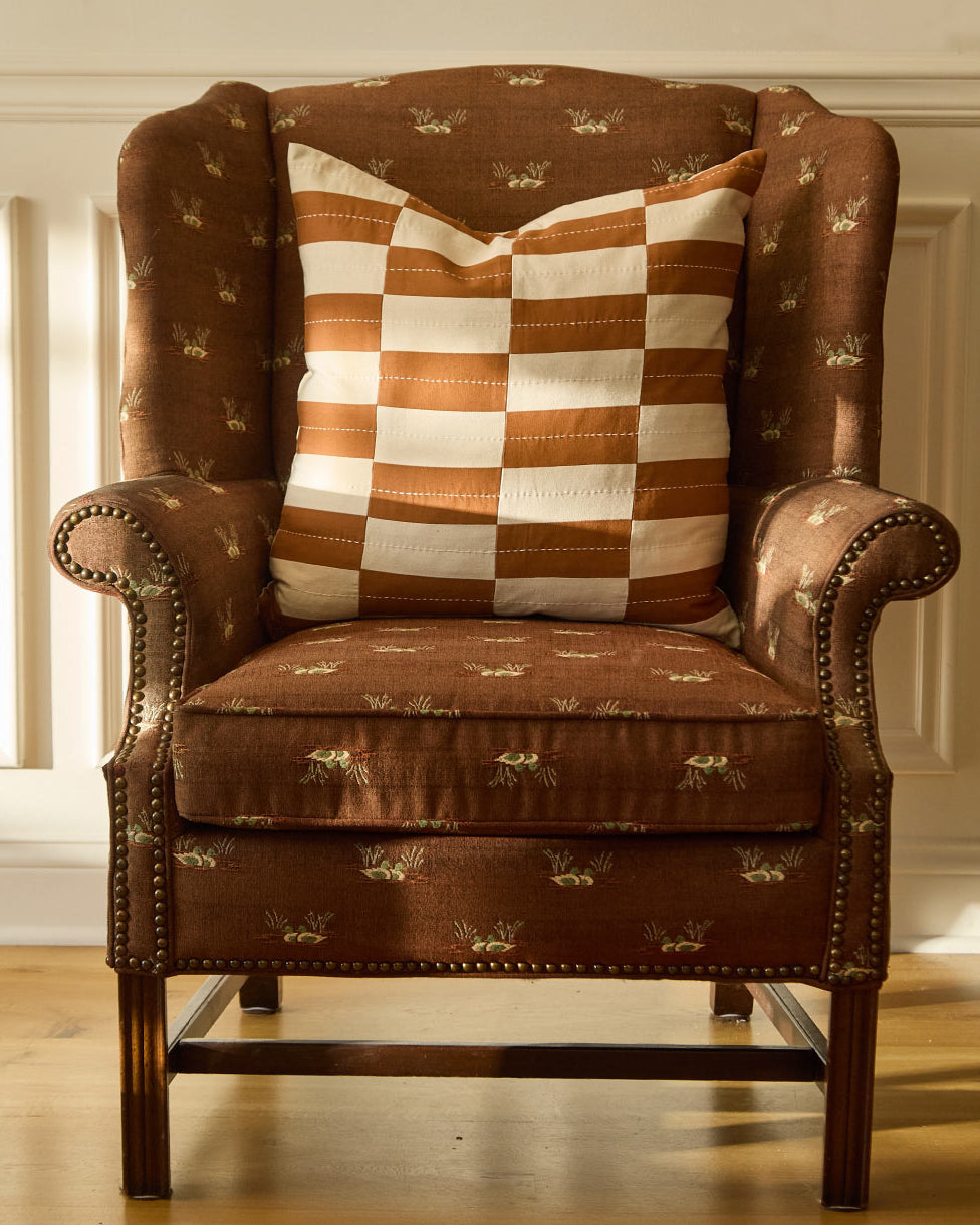 camel brown and white checkered pillow sitting on a vintage style brown upholstered chair