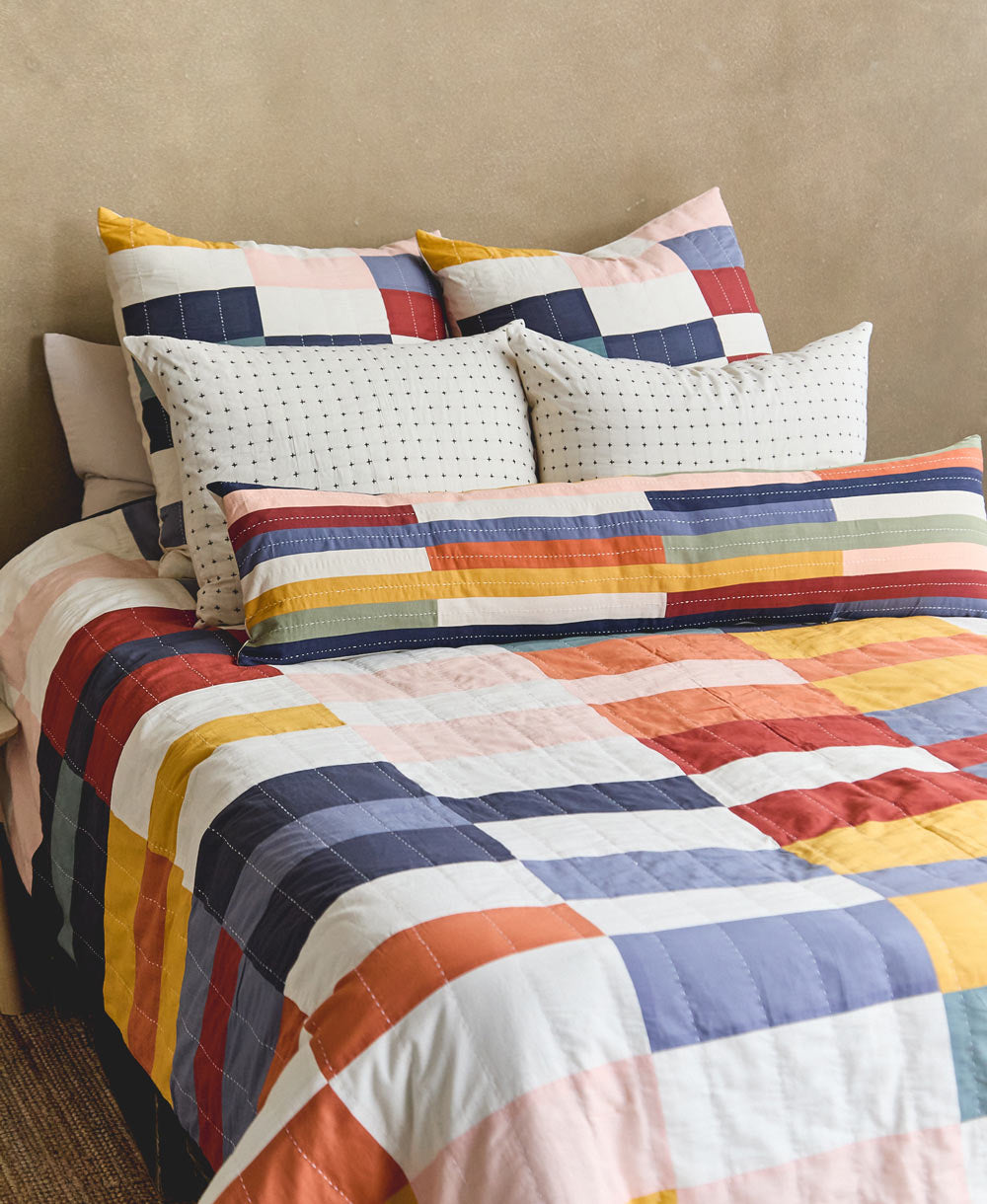 Colorful patchwork quilt with patterned throw pillows on a bed against a beige wall