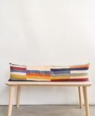 Colorful striped long lumbar pillow on a wooden bench against a white wall