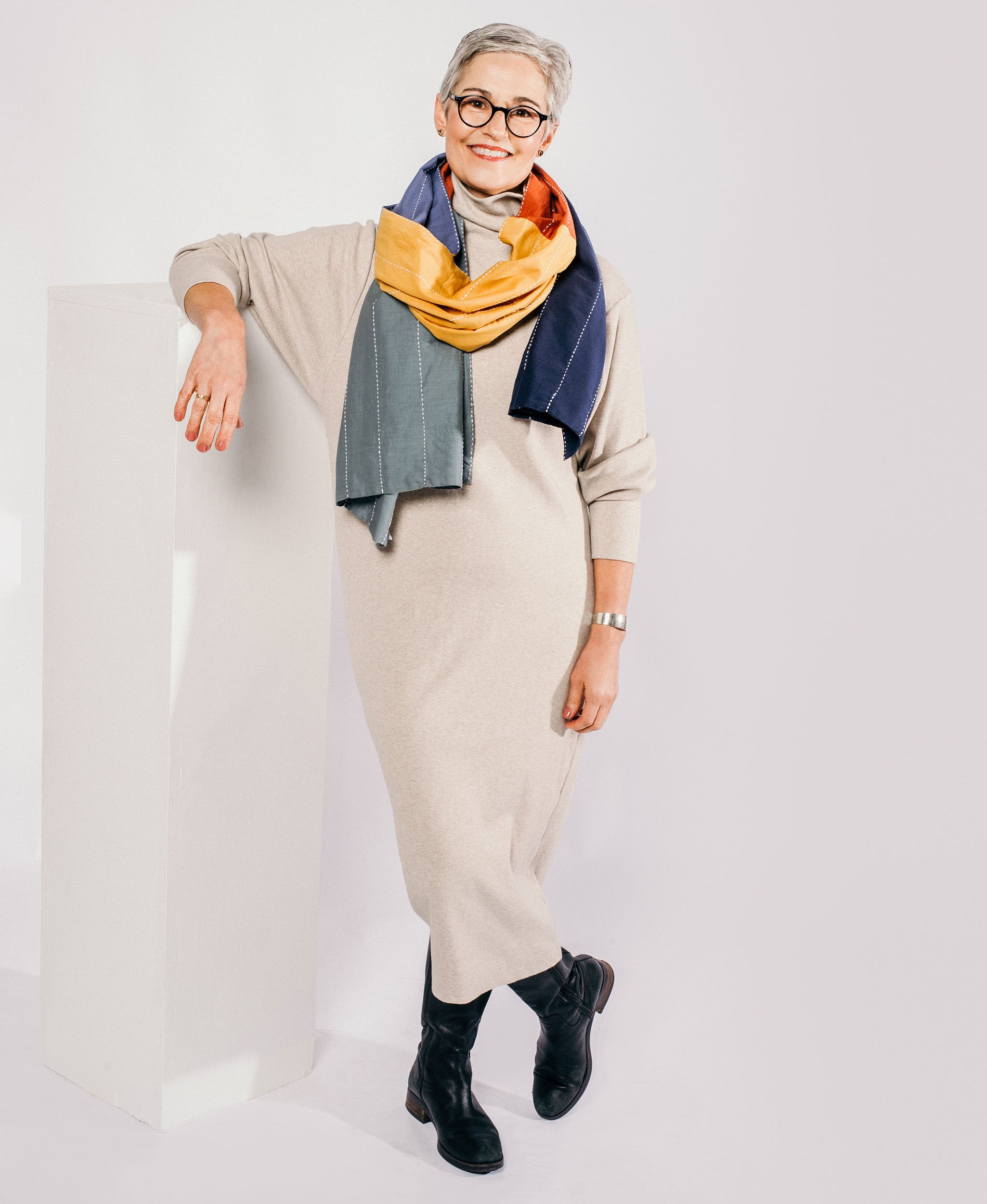 woman wearing rainbow long scarf in neutral sweater dress and black boots