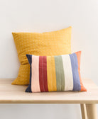 Two colorful pillows on a wooden bench against a white wall