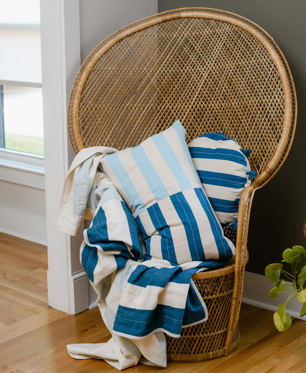 Wicker chair with a blue and white striped blanket draped over it in a room with a window.