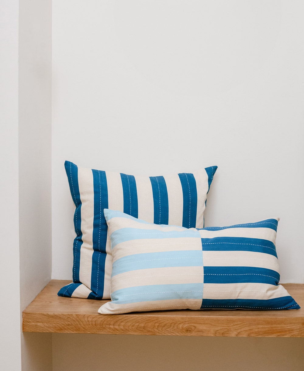 Two blue and white striped pillows on a light wooden bench against a white wall