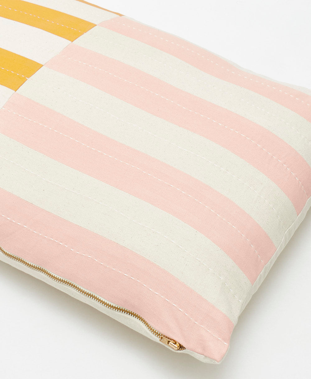 pink and white striped pillow with gold zipper on a light background