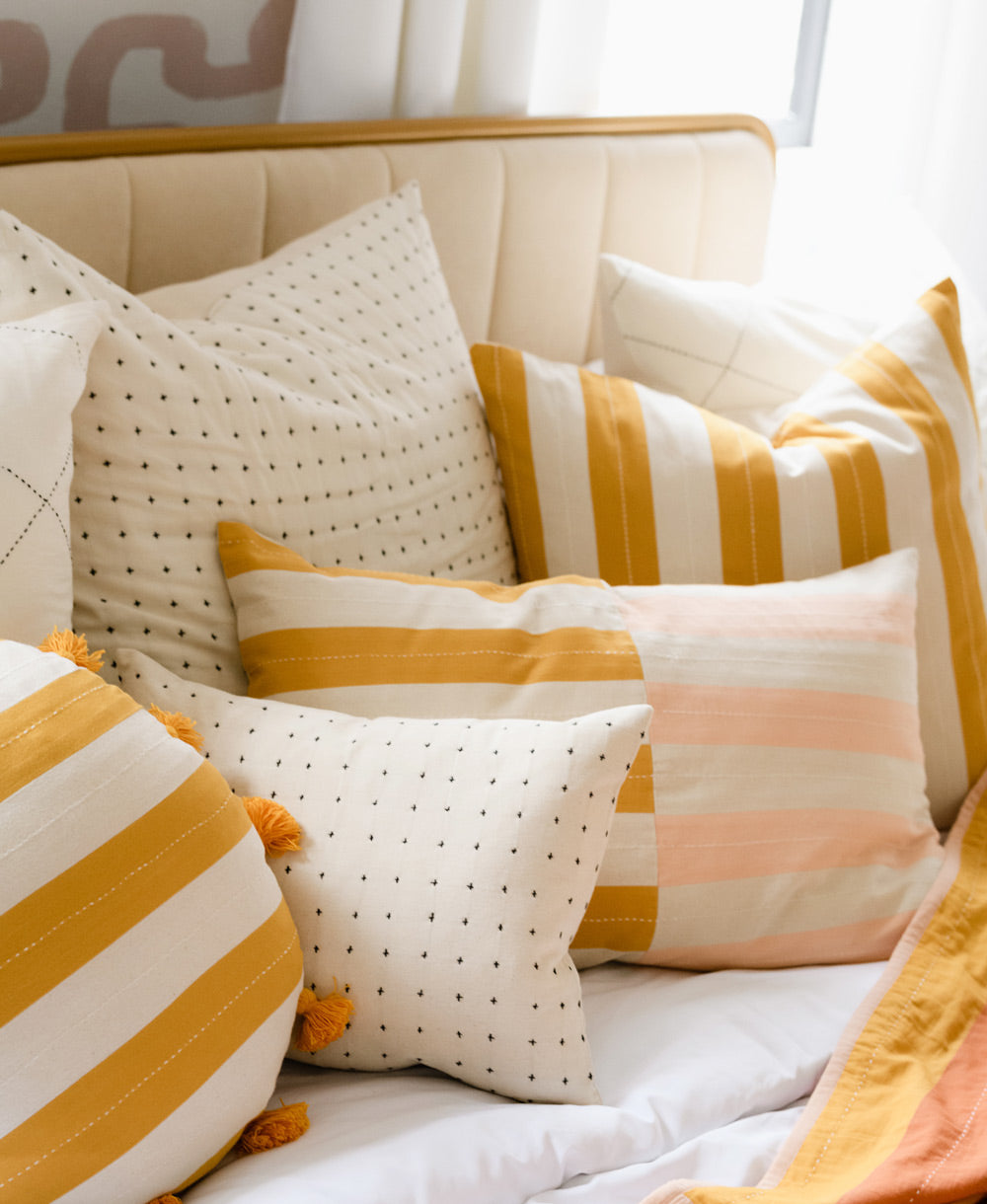 Decorative pillows with yellow and white stripes on an all white bed with a cream velvet and gold headboard