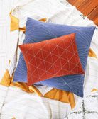 Two quilted pillows, one blue and one red, on a quilt with geometric patterns