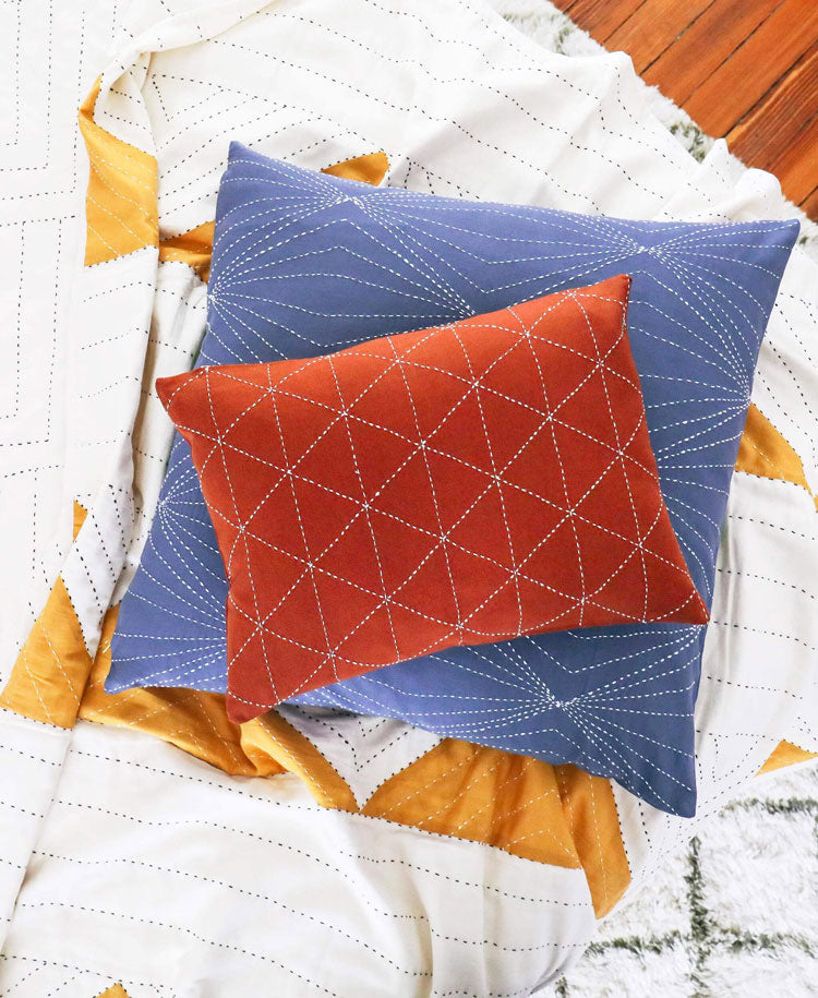 Two quilted pillows, one blue and one red, on a quilt with geometric patterns