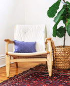 Wooden chair with a purple pillow next to a plant on a patterned rug