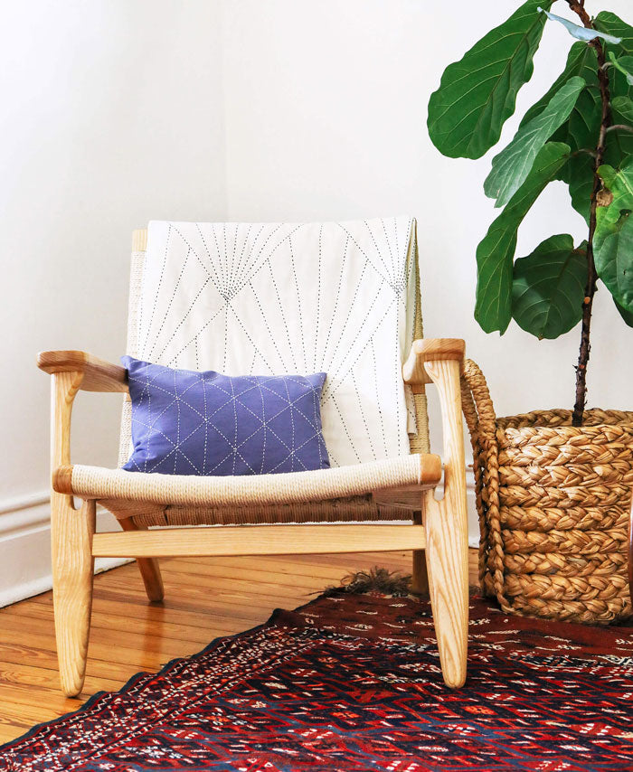 Wooden chair with a purple pillow next to a plant on a patterned rug