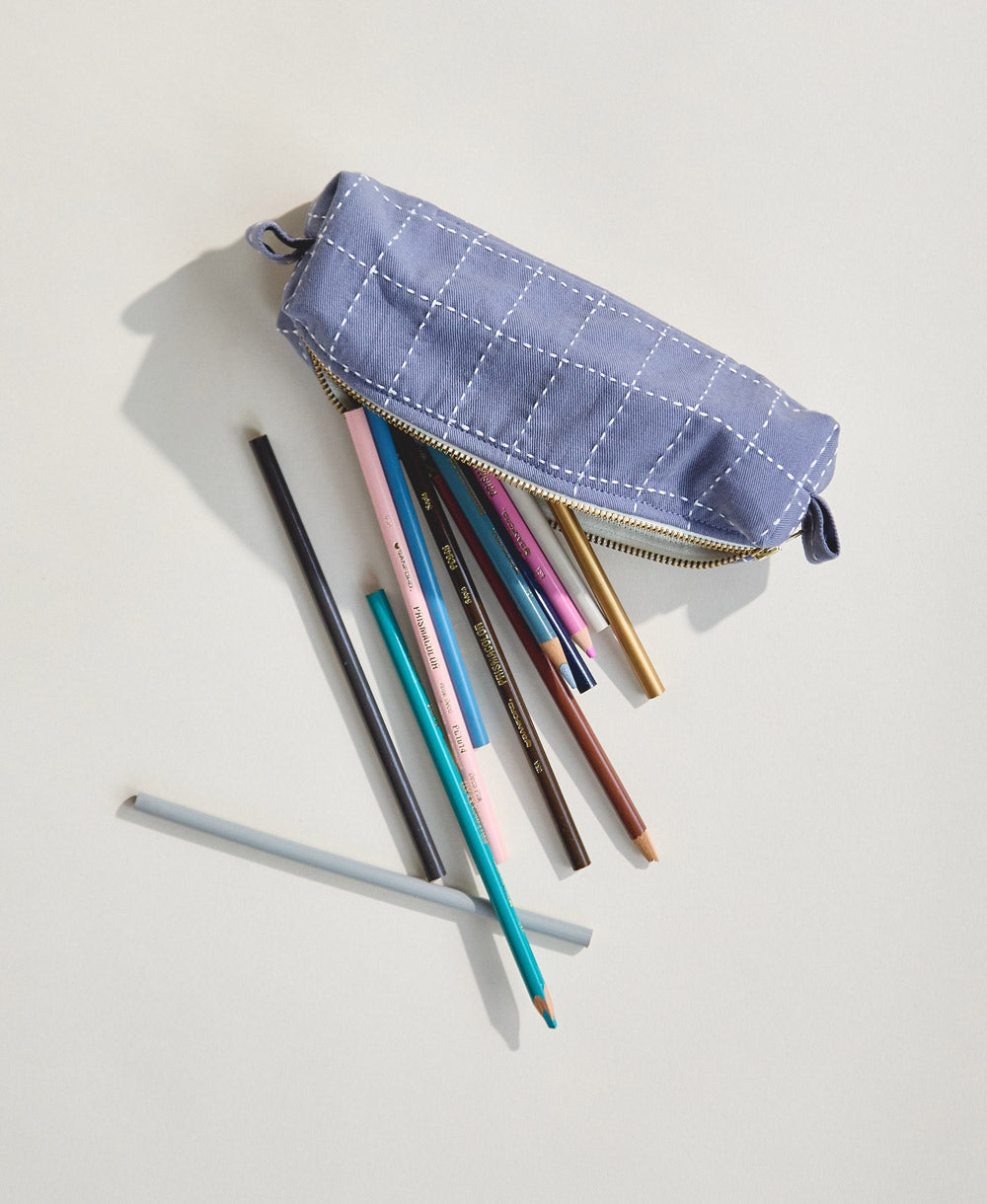 slate blue grid-stitch toiletry bag with pencils spilling out