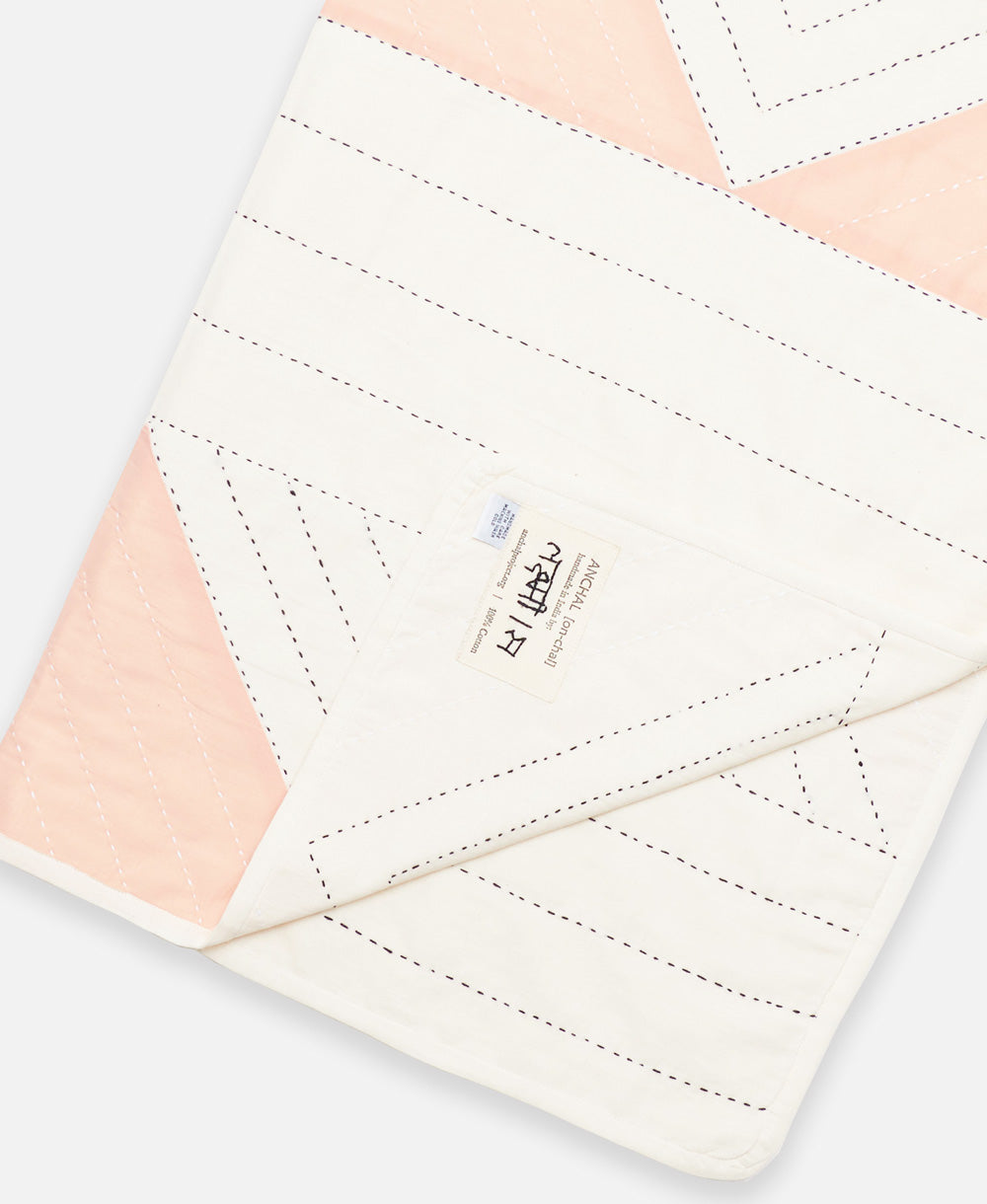 small triangle quilt throw in pink and off-white with artisan-signed tag on edge