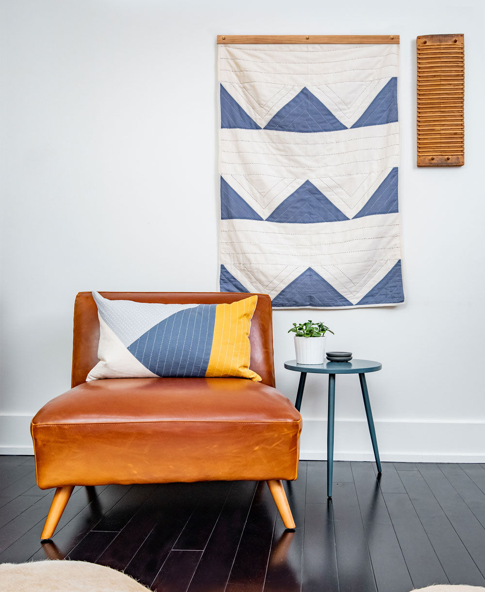 Brown leather chair with a colorful pillow in a room with a geometric tapestry on the wall.
