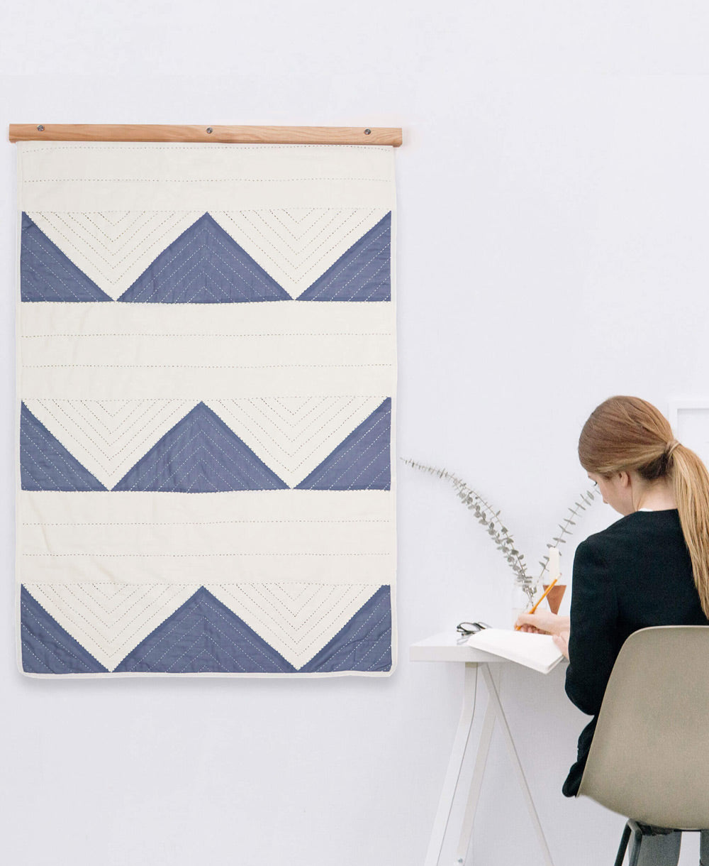 Person sitting at a desk with a blue and white geometric patterned wall hanging on a white wall.