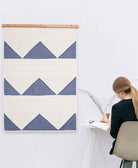 Person sitting at a desk with a blue and white geometric patterned wall hanging on a white wall.