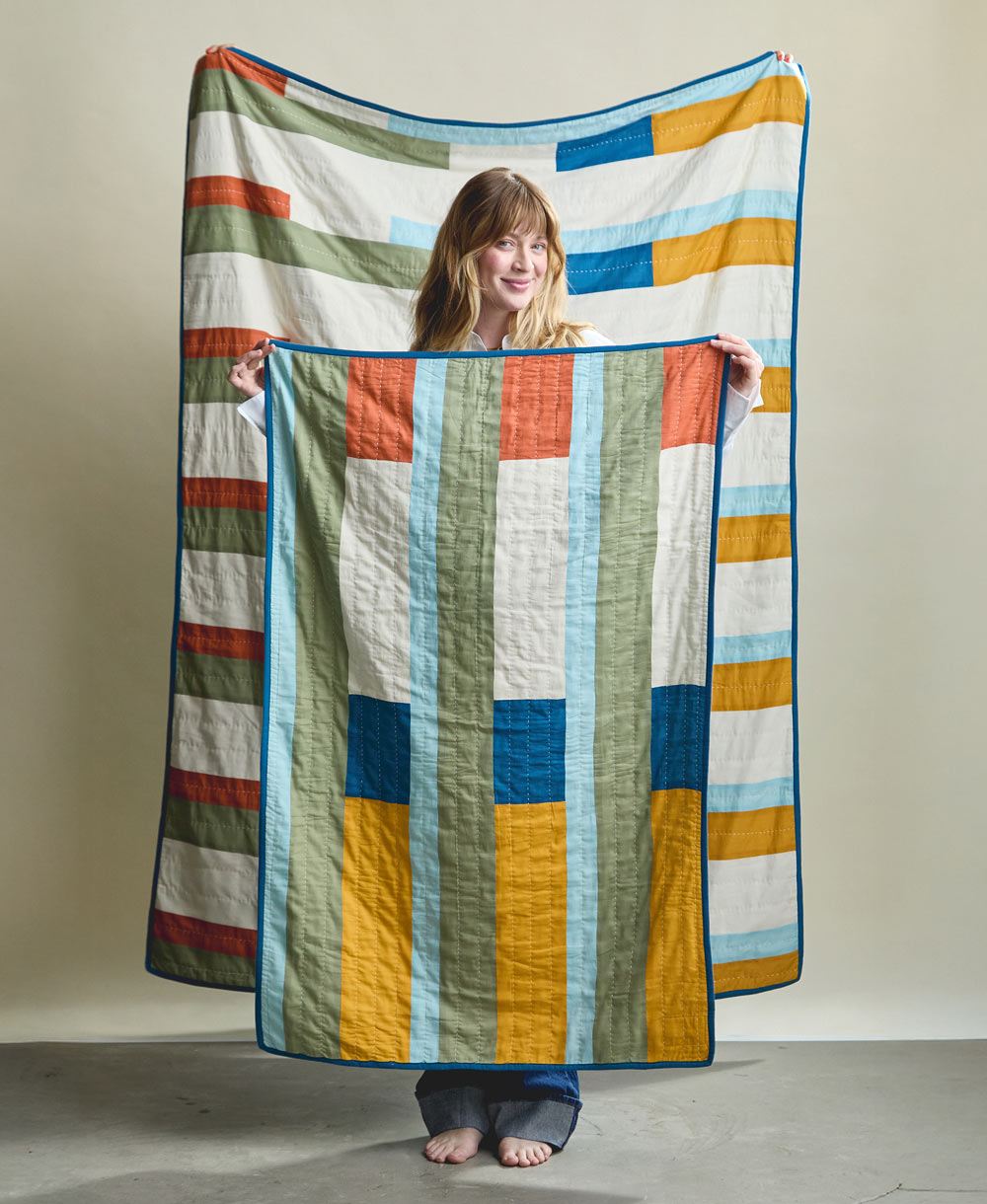 Woman holding a colorful quilt with geometric pattern against a plain background