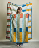 Woman holding a colorful quilt with geometric pattern against a plain background