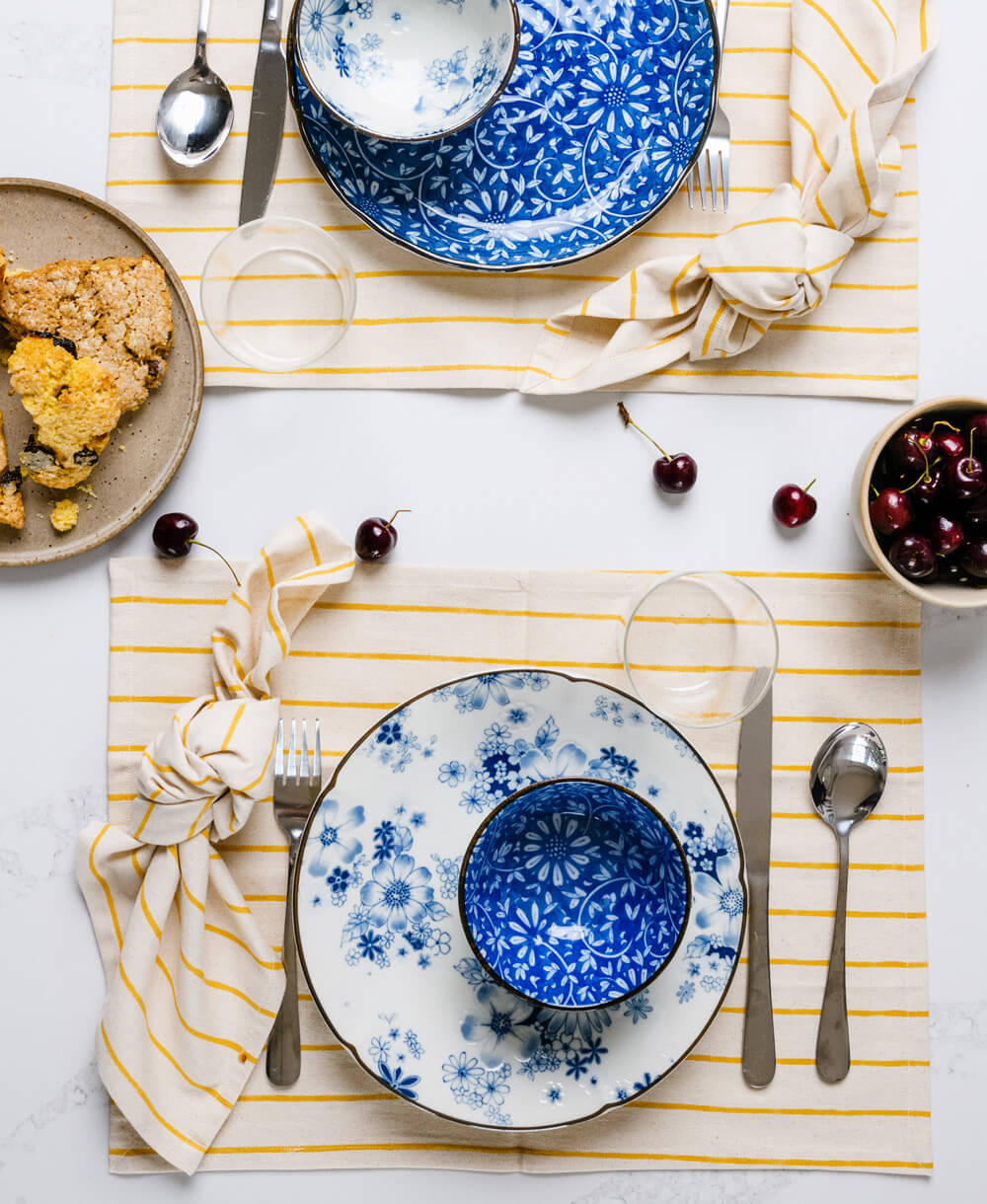 Dining table setting with blue floral plates, silverware, and a striped yellow and white napkin