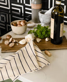 Wine bottle, mushrooms, and herbs on a kitchen counter with a striped navy blue cotton napkin
