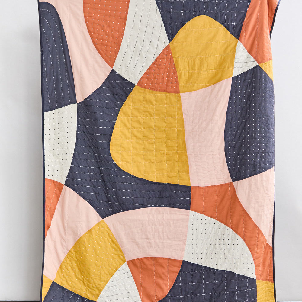 modern patchwork quilt in bold abstract shapes in yellow, navy, orange, pink and ivory