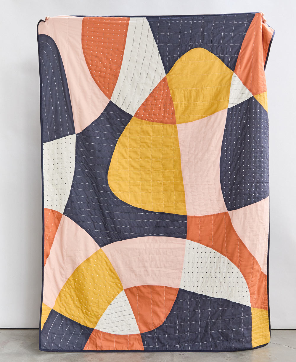 modern patchwork quilt in bold abstract shapes in yellow, navy, orange, pink and ivory