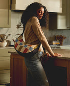 woman wearing checkered crescent bag standing in modern kitchen with warm wood tones