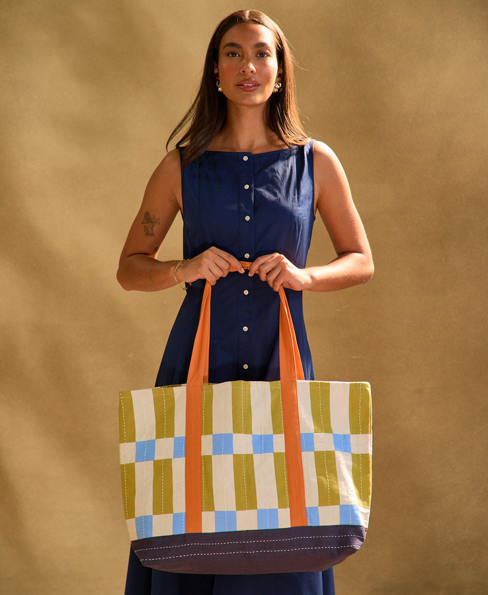 woman holding checkered canvas tote bag in blue, olive green, sky blue and orange while wearing blue dress
