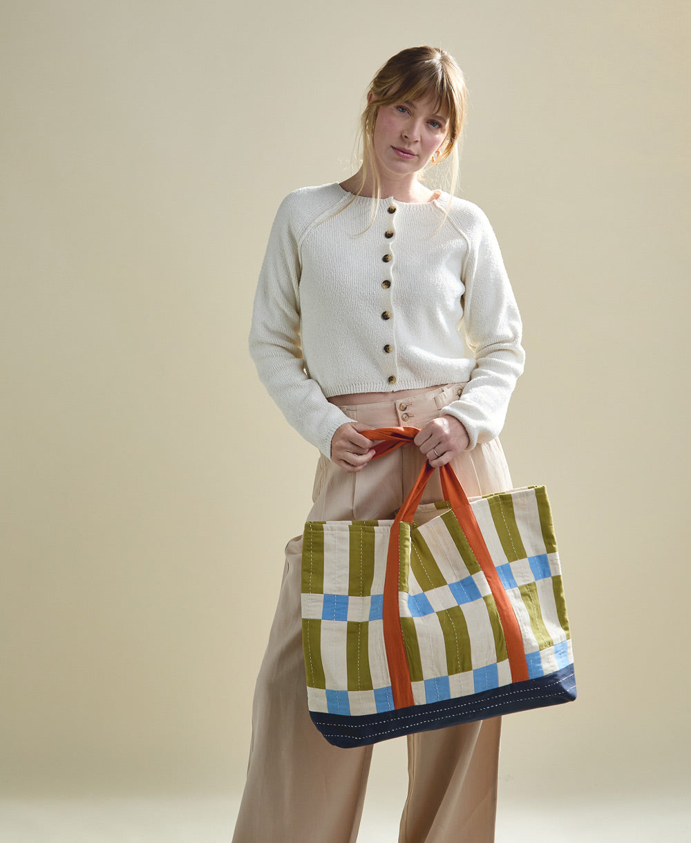 woman holding checkered canvas tote bag in bold checkered print with orange straps