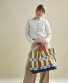 woman holding checkered canvas tote bag in bold checkered print with orange straps