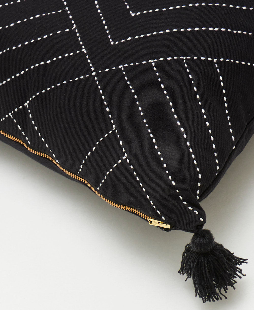 detail of tilt throw pillow in black with tassel on corner and brass-tone exposed metal zipper closure