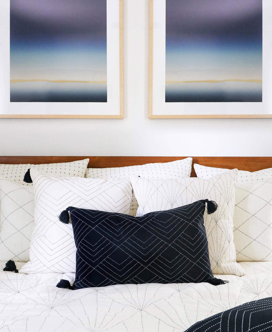 all white bed with two photos hung on the wall in the background with modern black throw pillow in a lumbar shape
