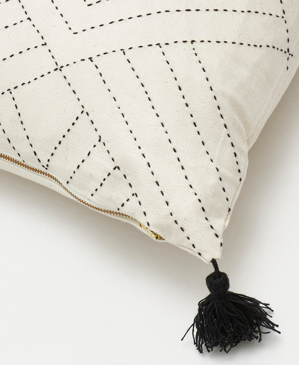 White pillow with black stitching and a black tassel on a white background