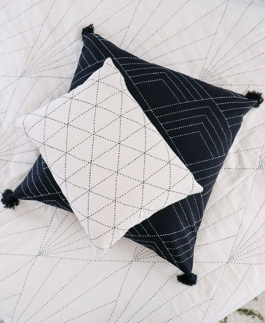 Two geometric-patterned pillows on a quilted surface