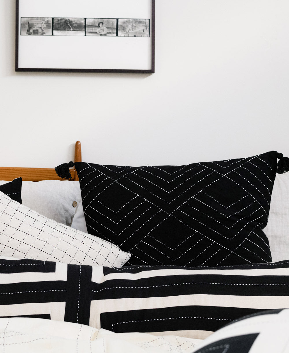ethically made black throw pillow on black and white bed with white embroidery